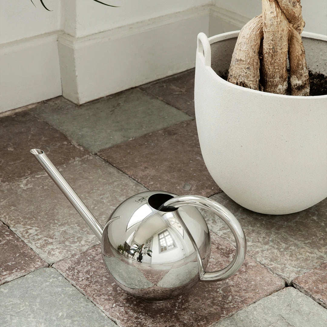 A Ferm Living Orb Watering Can with a handle on a tiled floor.