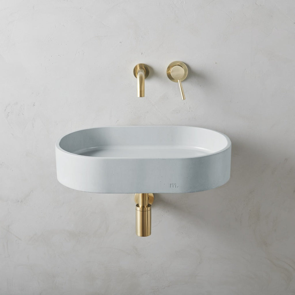 A mudd. concrete Parro Basin LG Affix with a gold faucet and a white wall.