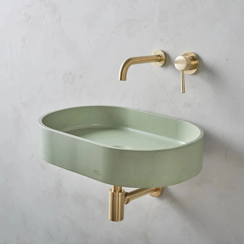 A Parro Basin LG Affix from mudd. concrete with a gold faucet and a green bowl.