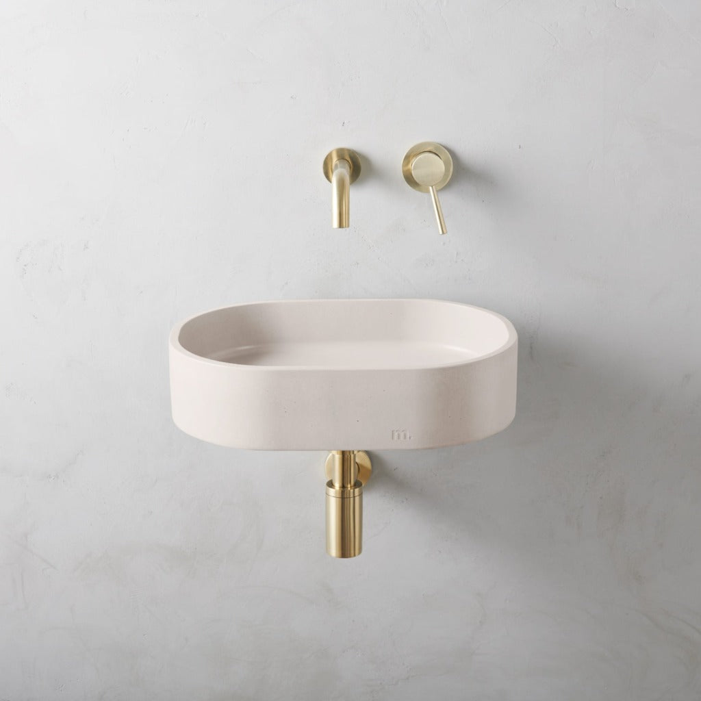 a mudd. concrete Parro Basin SM Affix with a gold faucet and a white wall.