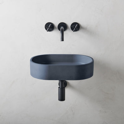 A Parro Basin SM Affix by mudd. concrete with a black faucet and two black soap dispensers.