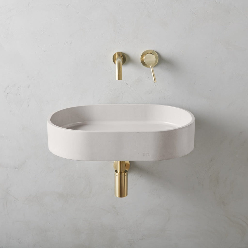 A white Parro Basin LG Affix from mudd. concrete with a gold faucet on the wall.