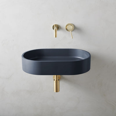 A Parro Basin LG Affix from mudd. concrete with a gold faucet and a blue bowl.