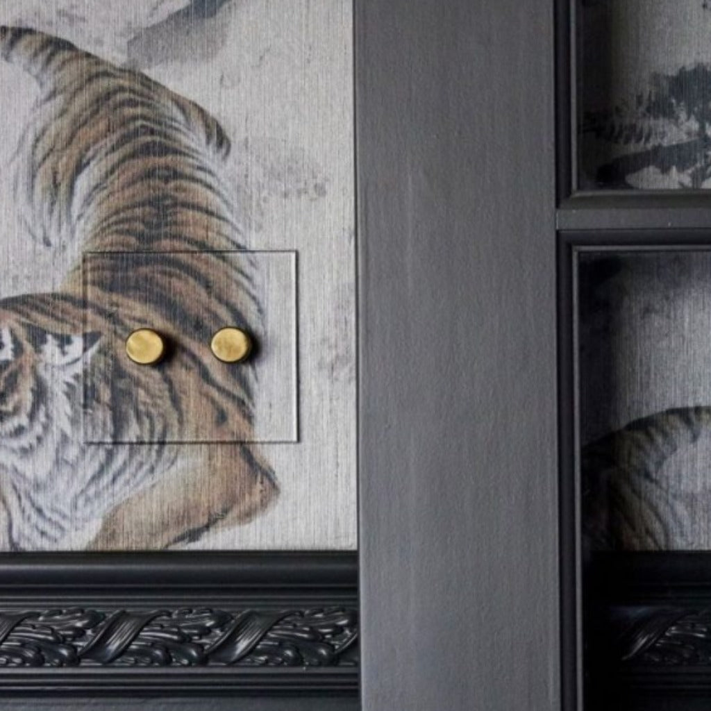 Forbes & Lomax invisible plate with brass dimmers on a wall with framed art.