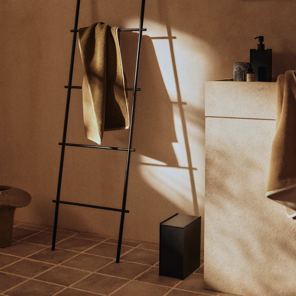 Black powder-coated steel Sama Bin with a minimalist, sculptural design in a modern bathroom setting.