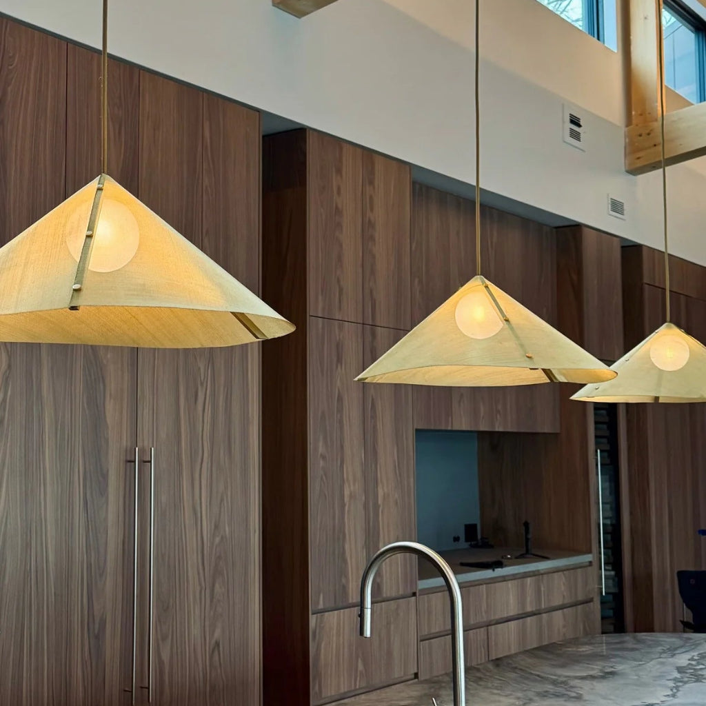 Modern cottage kitchen with pendant mesh screen lights, marble countertop, and wooden cabinets.