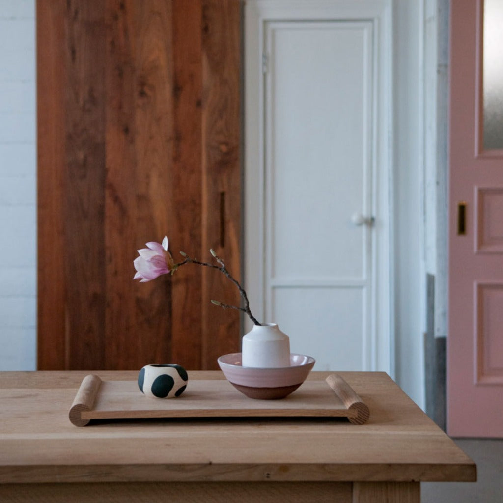 A rectangular wooden tray with a flower in a vase placed on top