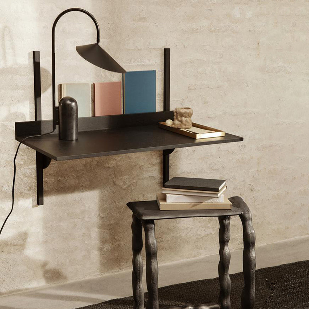 A Ferm Living Sector Desk with a lamp and books on it.