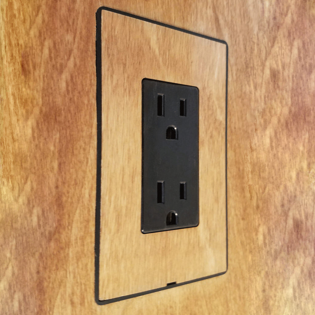 A wooden wall with a DesignMod Smoothline Flush Mount Wall Plate: Alternate Material Mount for black electrical outlet.