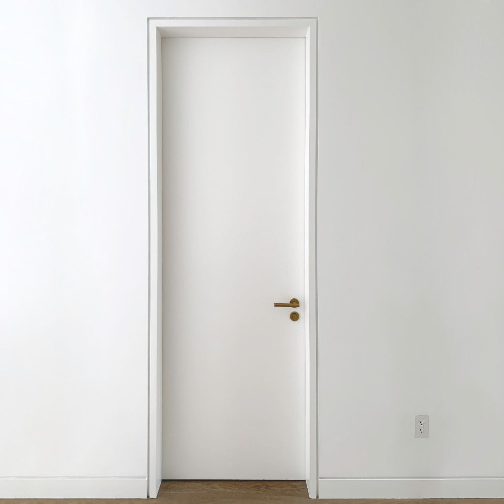 A minimal door with gold hardware in a white room with a wooden floor and a DesignMod Smoothline Flush Mount Wall Outlet Plate: Drywall Mount.