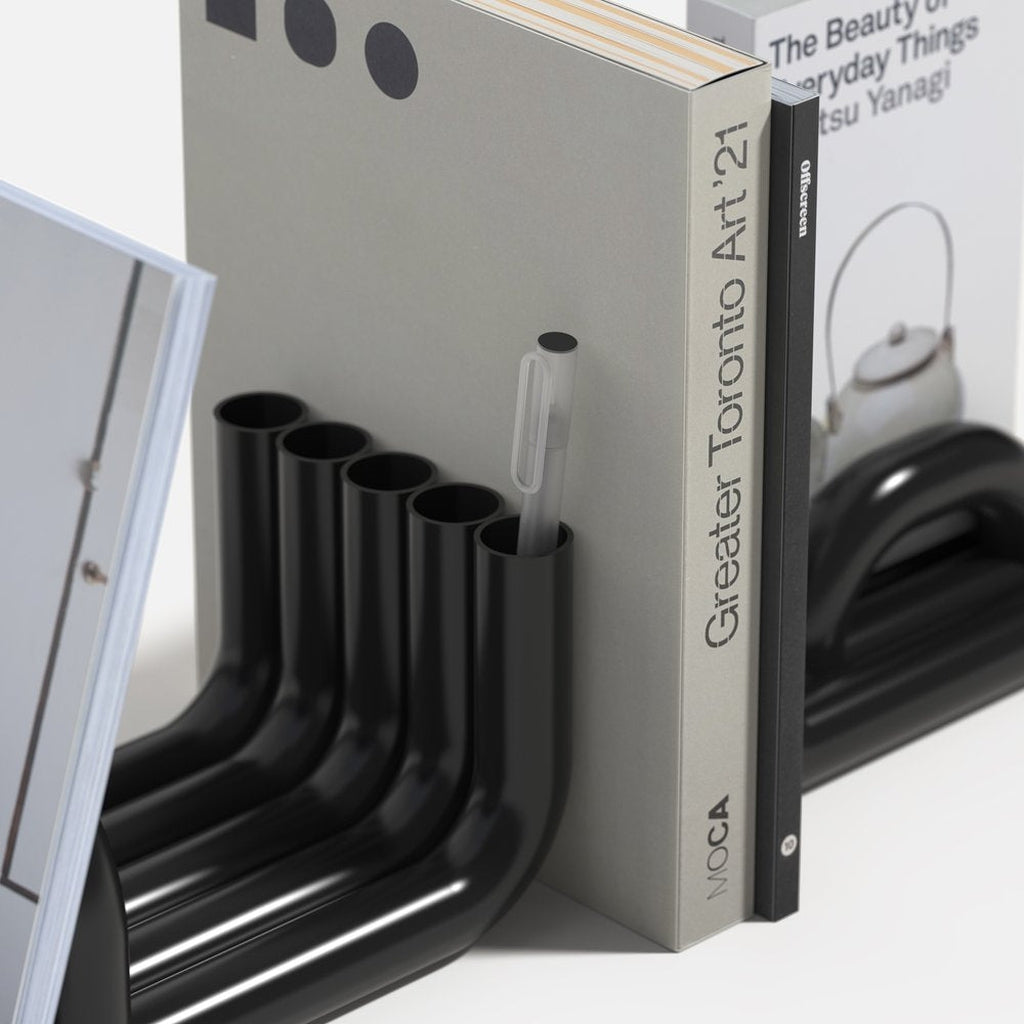 close up detail of Black TUBE Bookends photographed on a white background with a collection of books in between and pens in the tubes