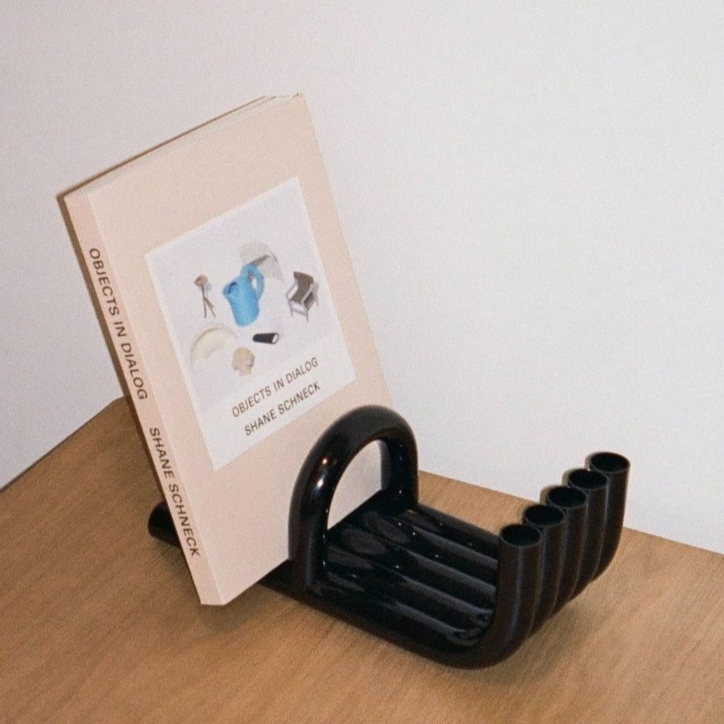 Black TUBE Bookends photographed on a wood table in a white room with a collection of books in between