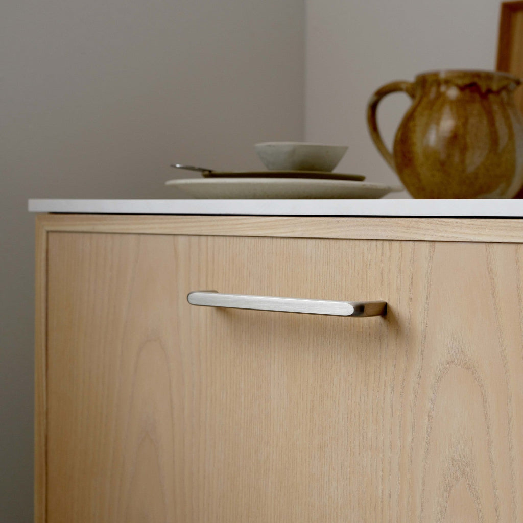 Inox look Furnipart Unify cabinet handle, 160 mm, on a light ash cabinet door under a white countertop.