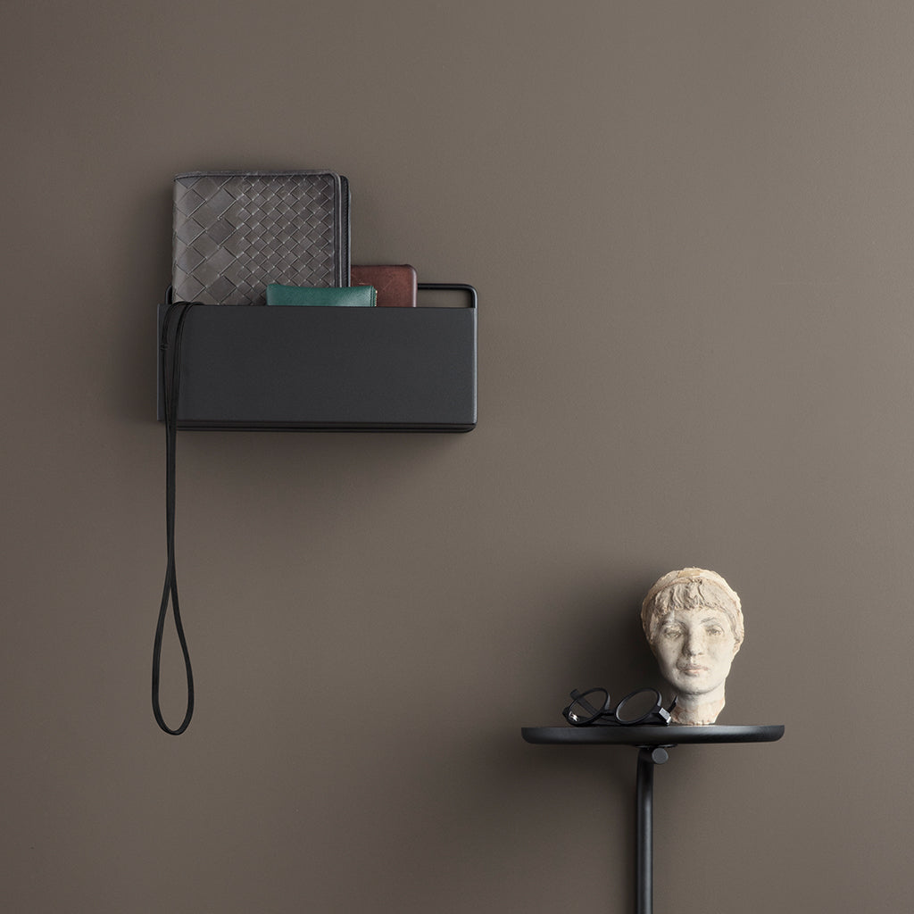 A Ferm Living Wall Box mounted on the wall next to a phone, with a sculpture of a head on the table below.