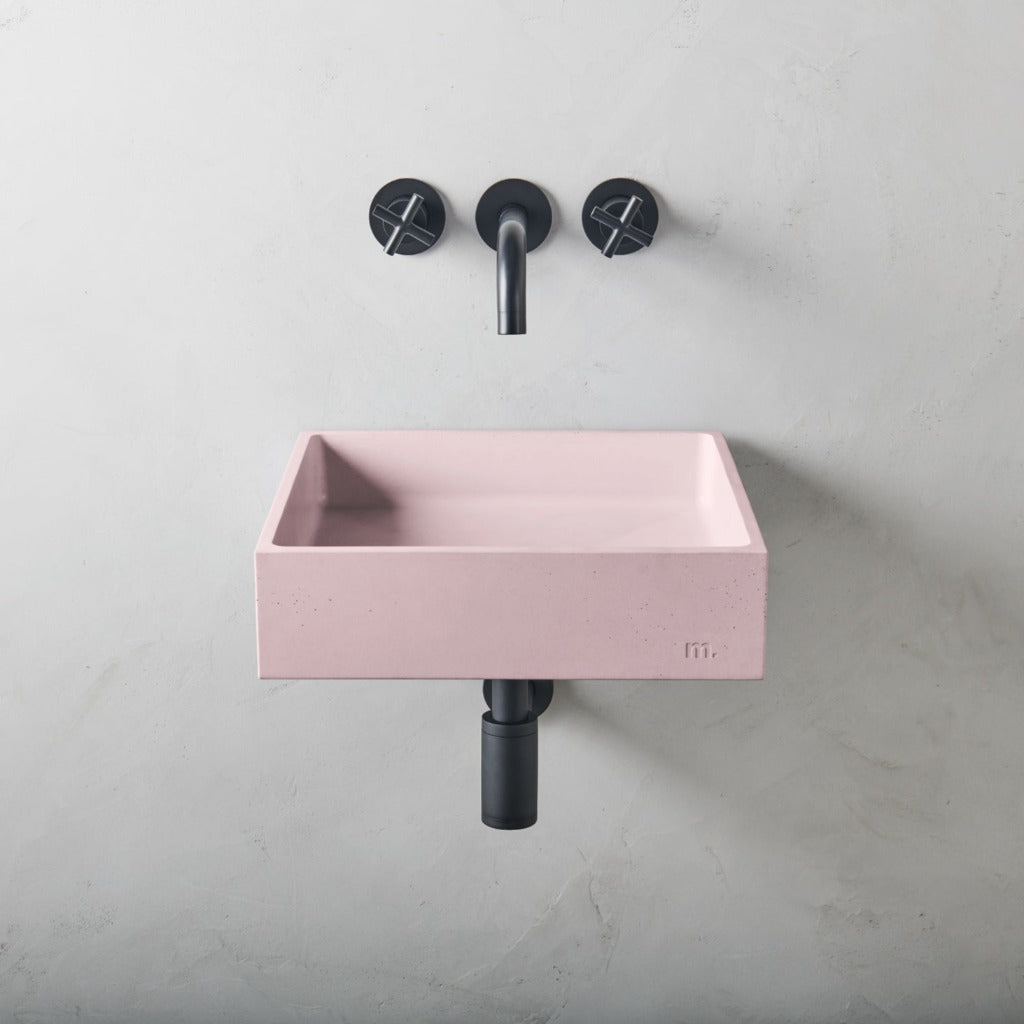 A pink Yarra Basin LG Affix sink with two black mudd. concrete faucets on the wall.