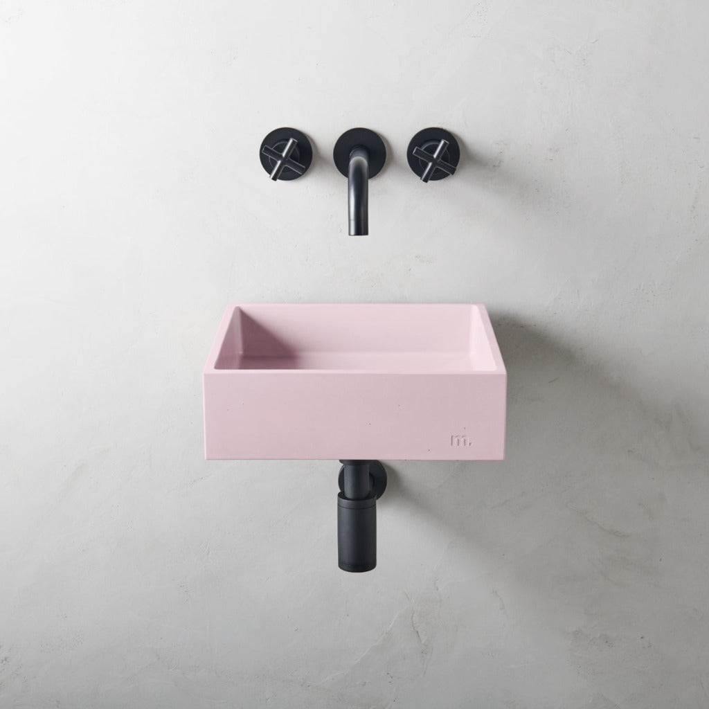A pink Yarra Basin SM Affix sink and two black mudd. concrete faucets on a white wall.