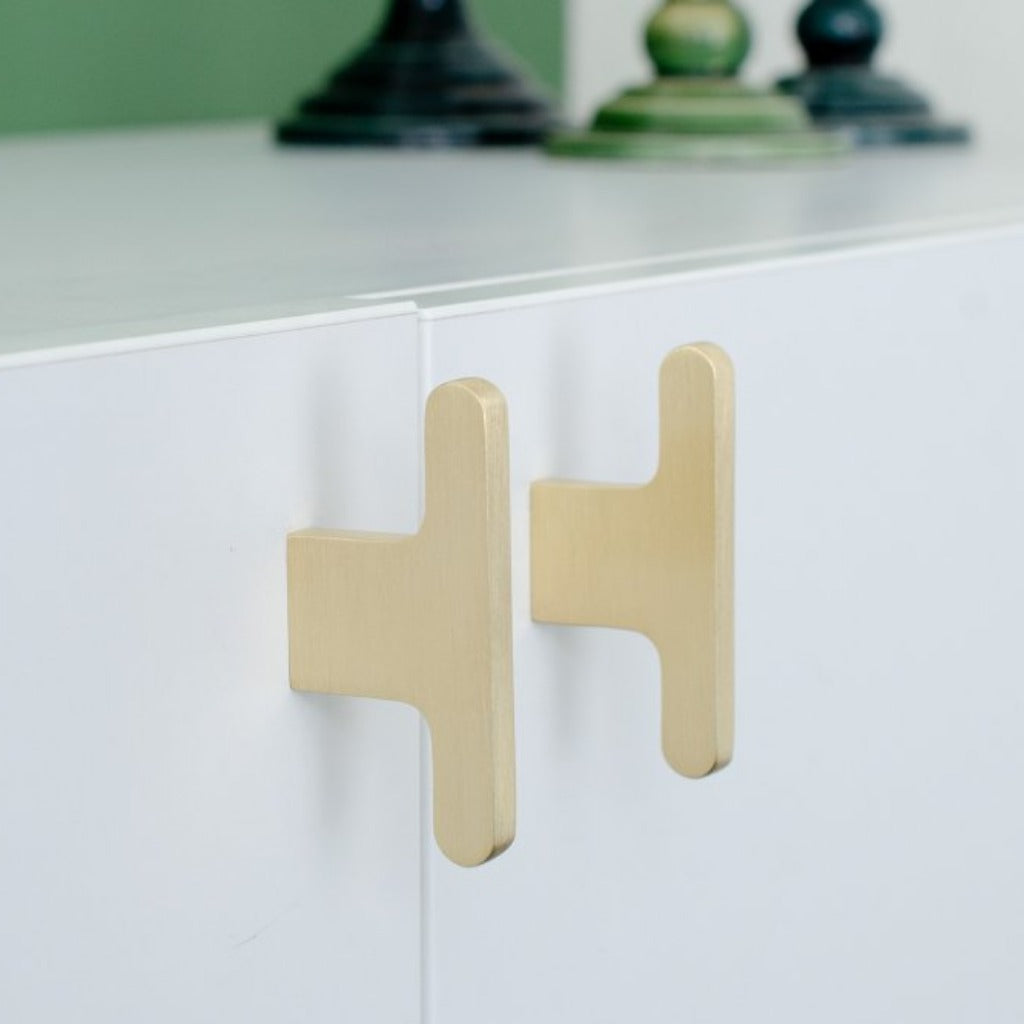 A T shaped knob in brushed brass mounted on a white cabinet