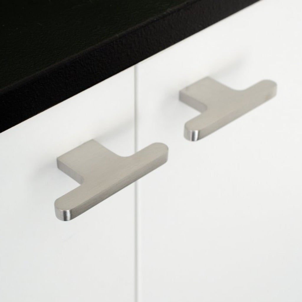 T shaped knobs in brushed stainless steel mounted on a white cabinet