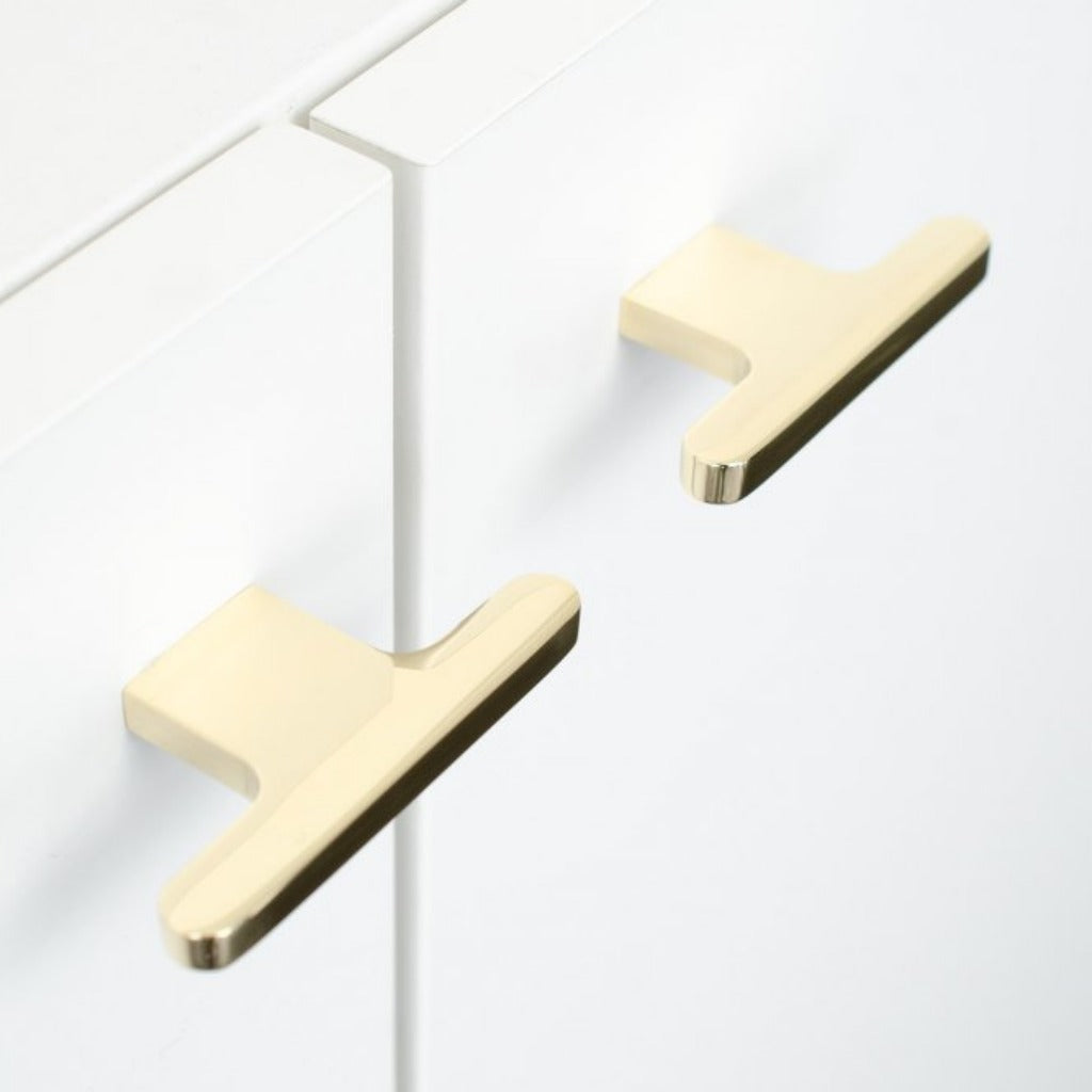 T shaped knobs in polished brass mounted on a white cabinet
