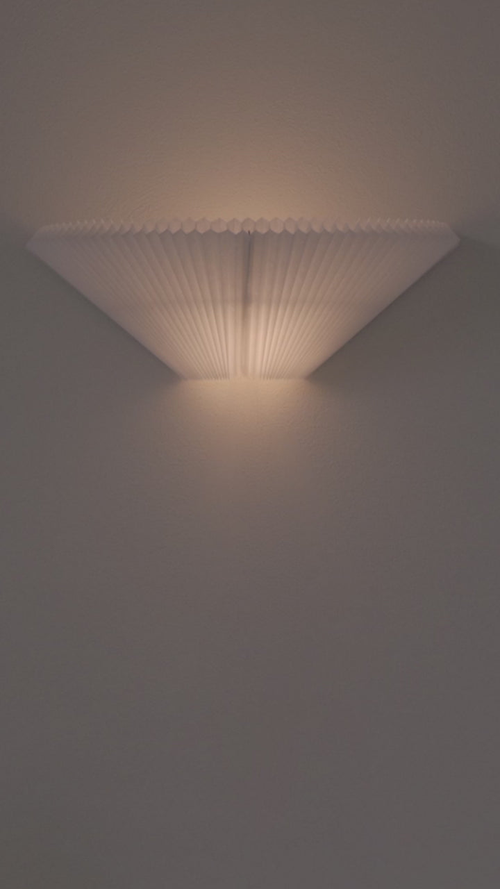 A short video of a white, pleated wall lamp being adjusted 