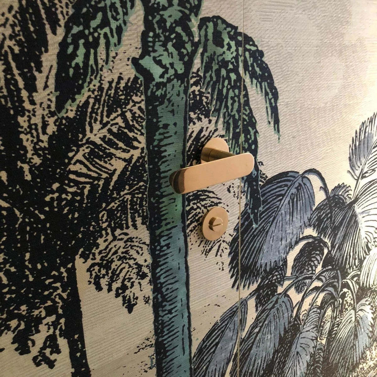 Copper Vervloet Audrey door lever on a botanical mural door.