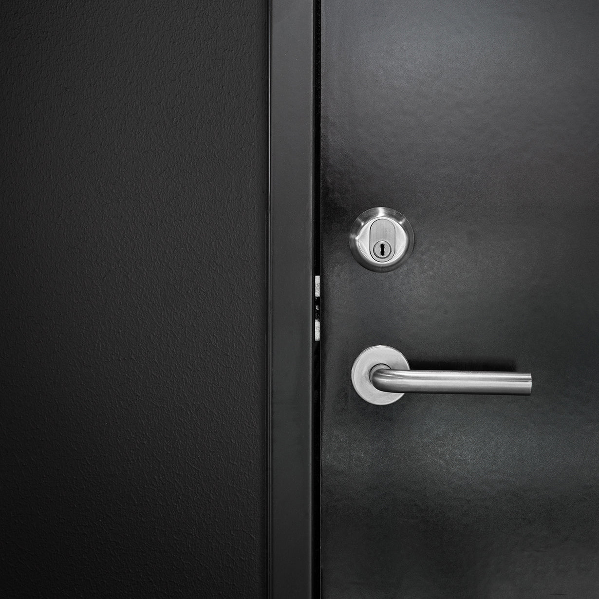Knud L Lever in satin stainless steel installed on a black industrial door with a Knud keyed lock.